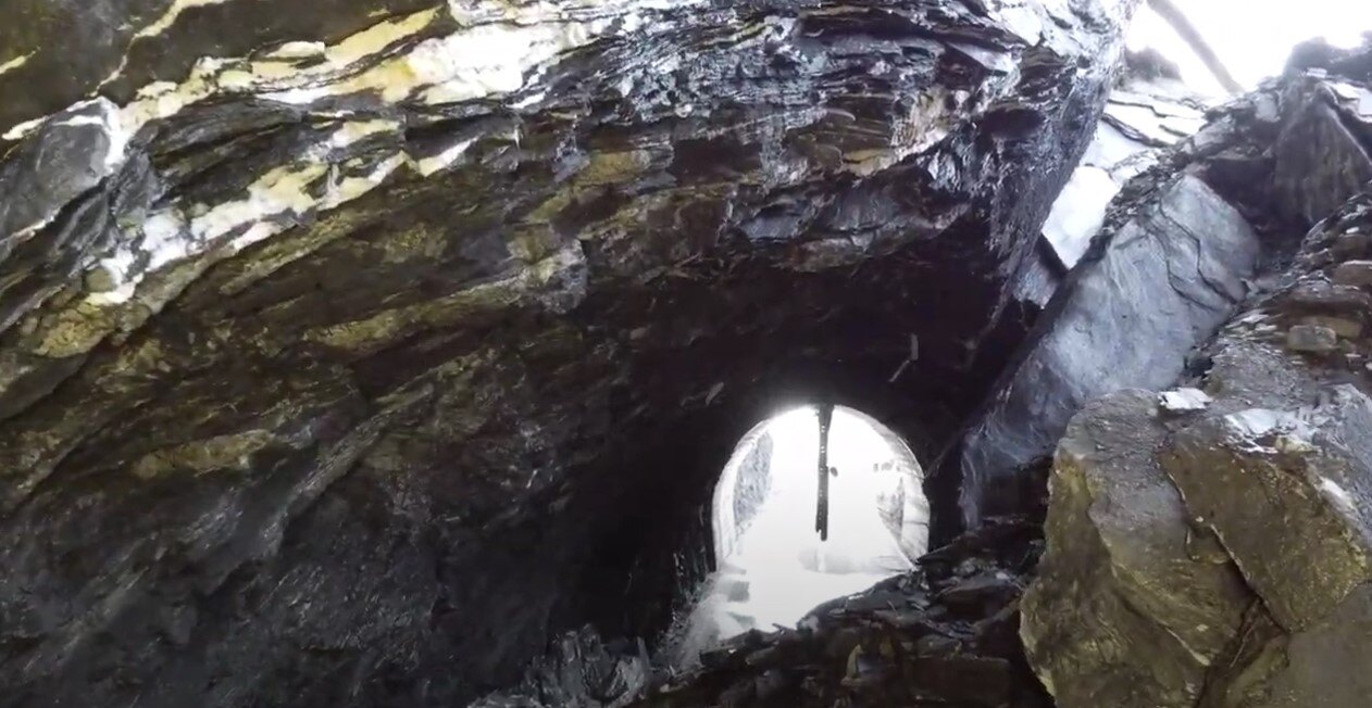 Photo of rocks piled high in side the collapsed tunnel, with tunnel opening visible beyond rockpile 