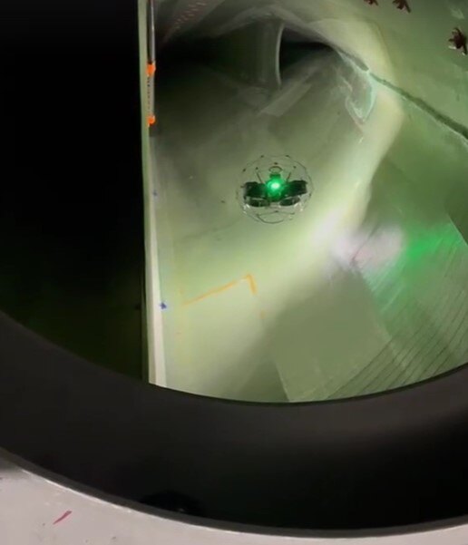 The Elios 3 flying inside a wind turbine blade which is a large, metallic space. The lights of the Elios 3 create a shadow effect around it 