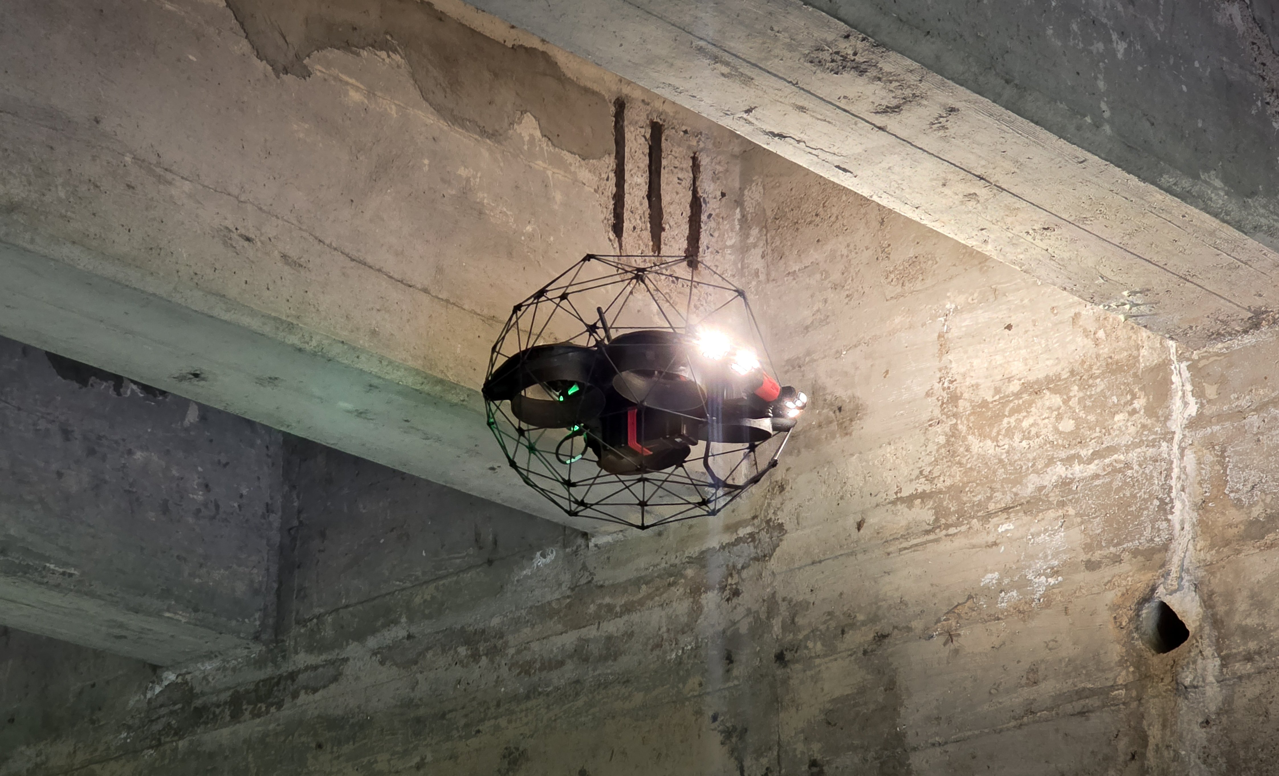 An Elios 3 drone in the hair flying underneath parallel concrete columns that make up the underside of a bridge
