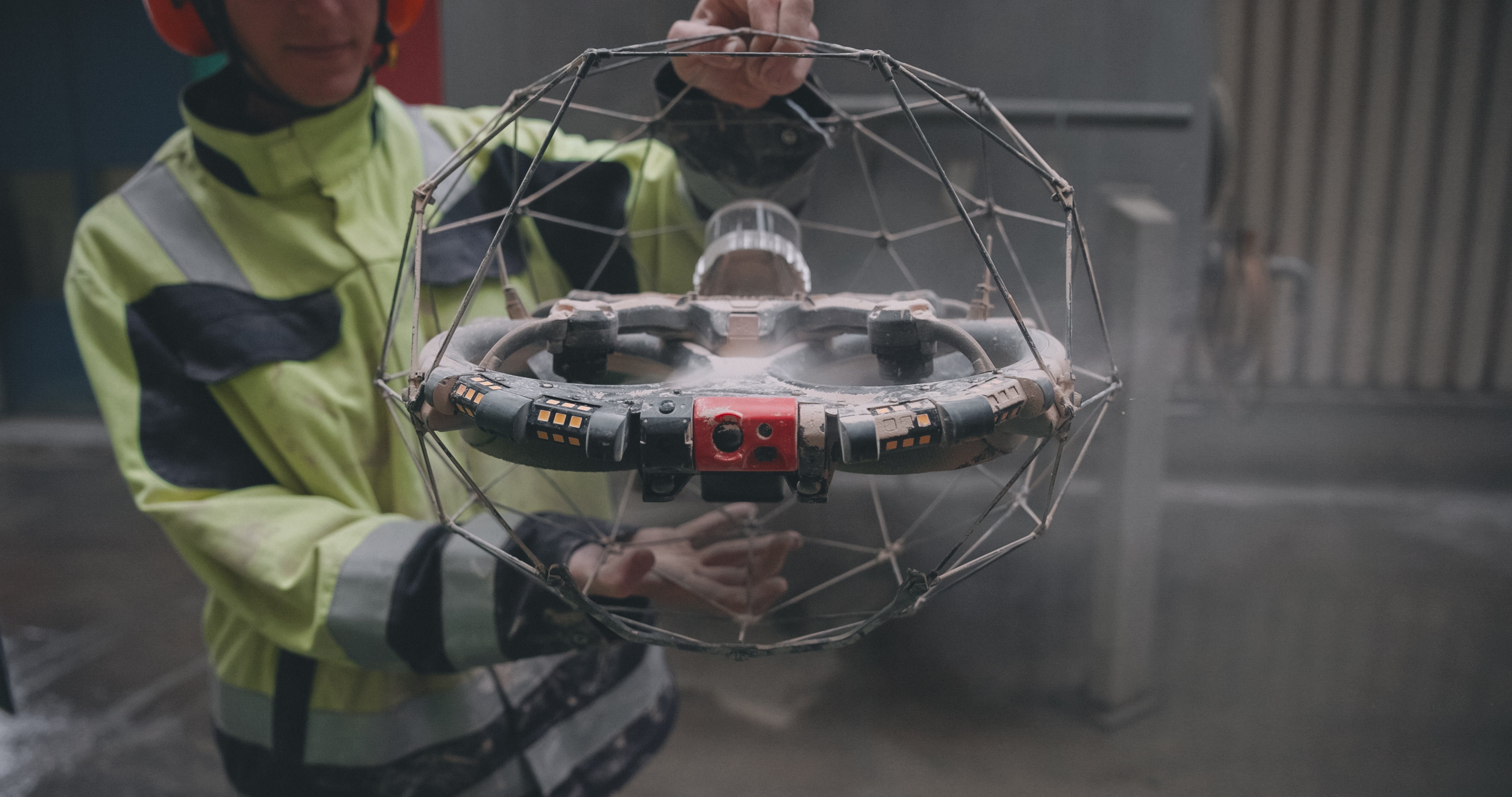 An Elios 3 pilot carrying the drone, which is covered in dust 